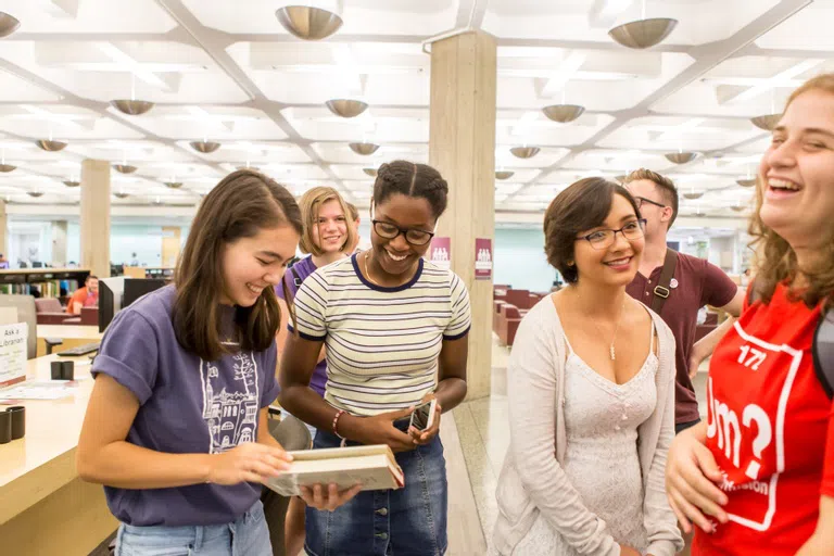 a group of students are gathered around reading a book in the library