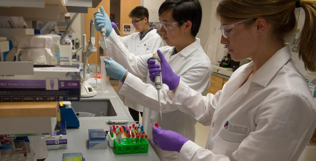 3 students in lab gear perform research in PME lab