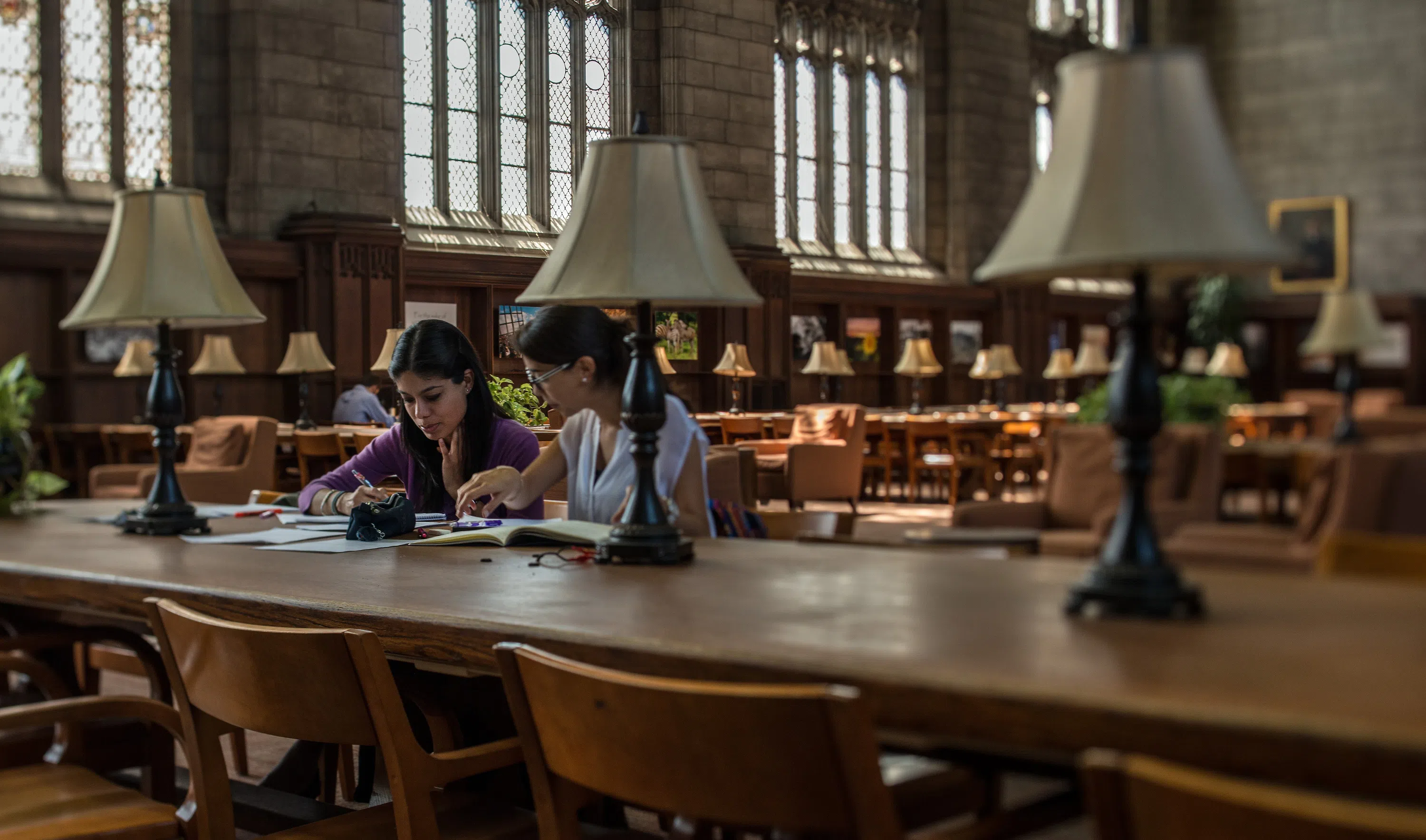 Two students sit side by side at a table in the reading room