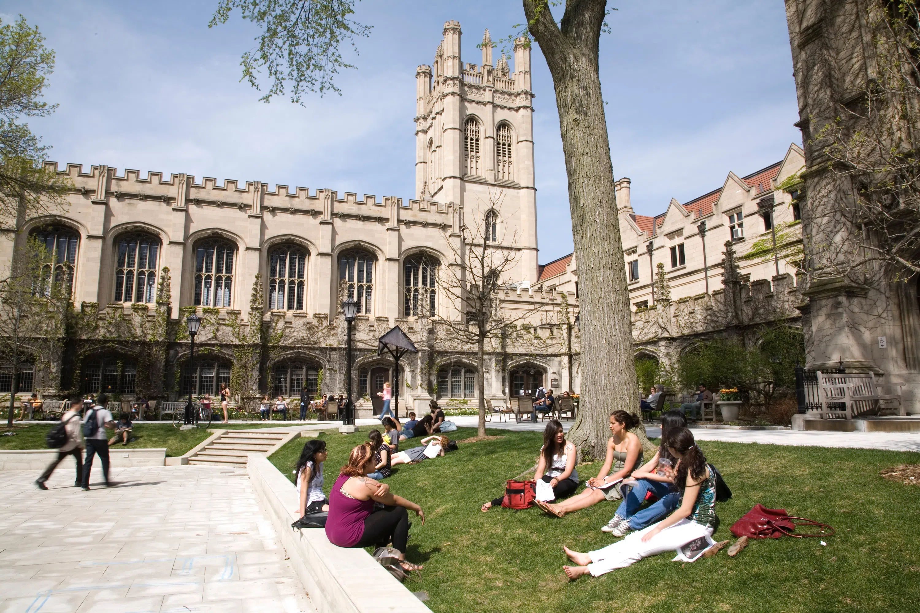 A group of students sit in a courtyard, with a Gothic-style building in the background