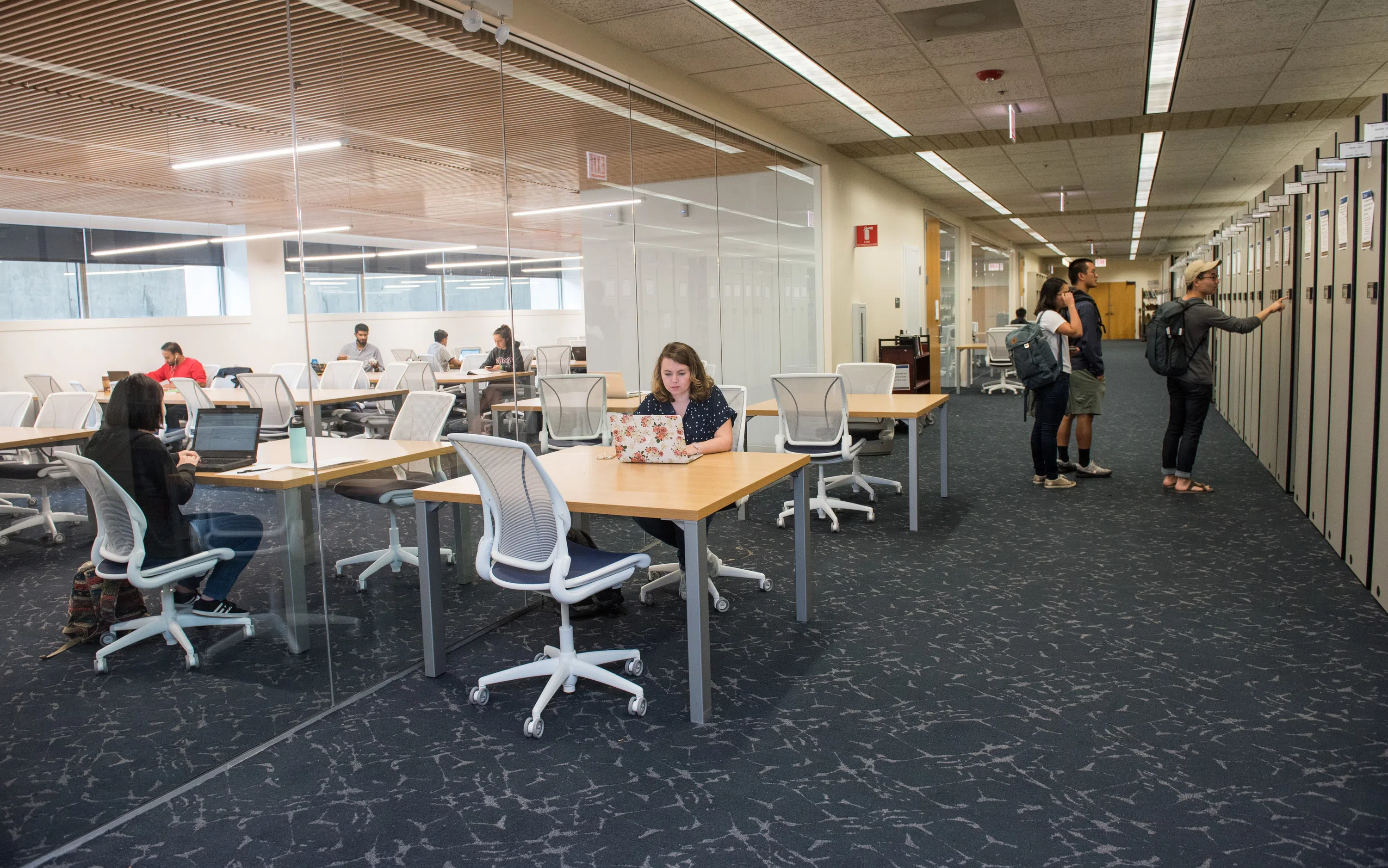 A student sits at a desk in Crerar library with a glass background behind her