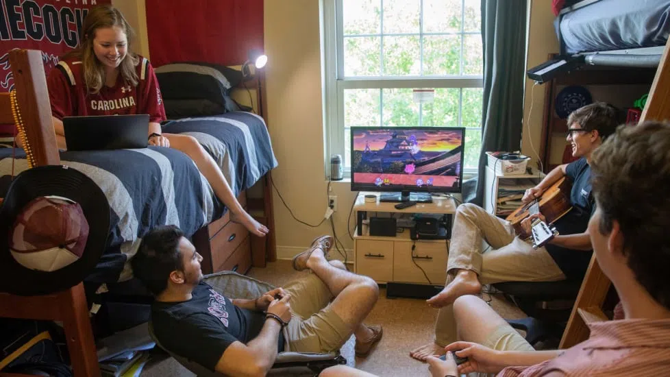 Four students relax and have fun together in a dorm room.