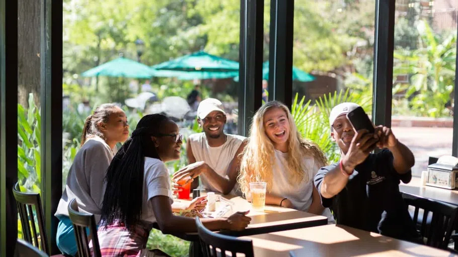 Group of students sitting together at a table and one of them is taking a selfie of the group