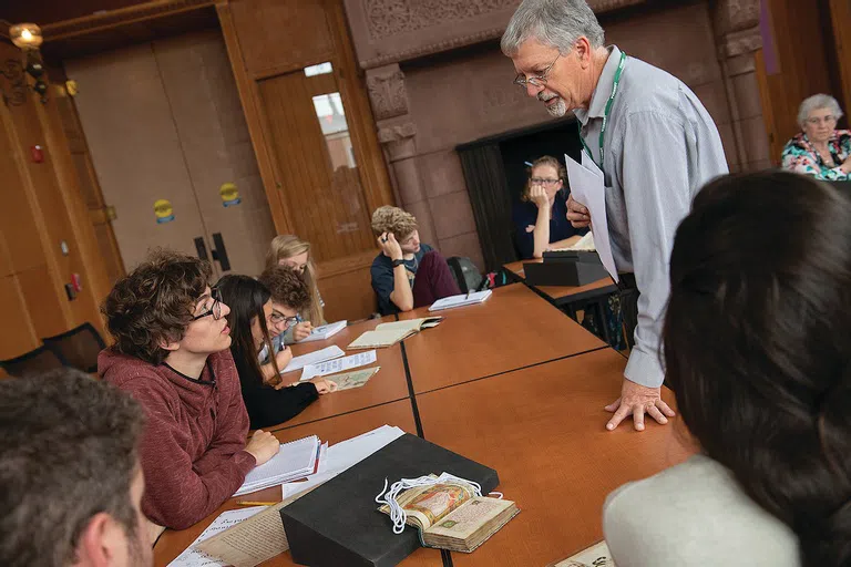 A professor standing at a table talking to a seated student.