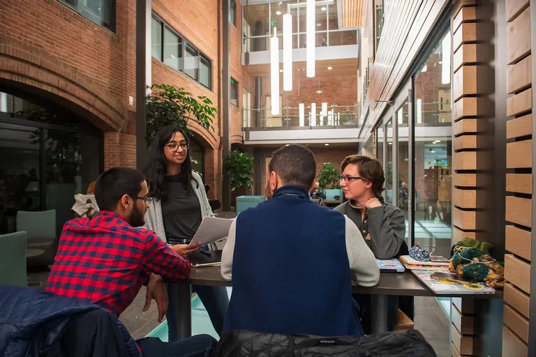 A group of four students standing and sitting around a table talking.