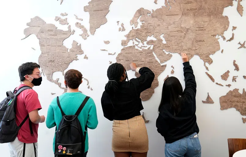 Four students place pins on a large wall map of the world to show where they are from.