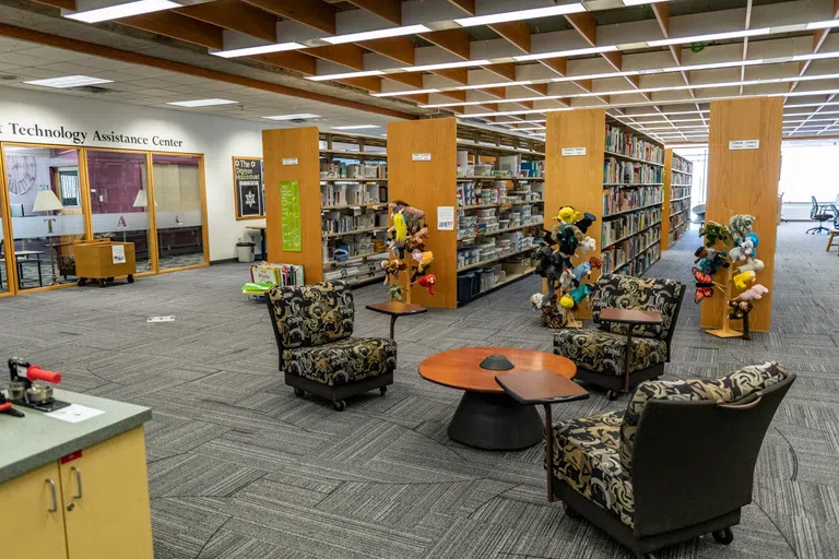 In the Educational Resource Center and the image shows seating, bookshelves of resources, the button making station, and puppets. The Technology Assistance Center is to the left. 