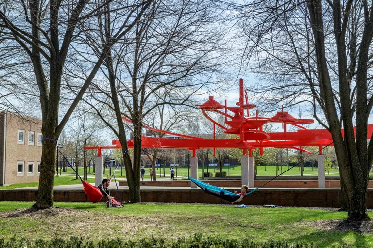 Two students lay in hammocks in front of the Turning Point sculpture at the center of campus.