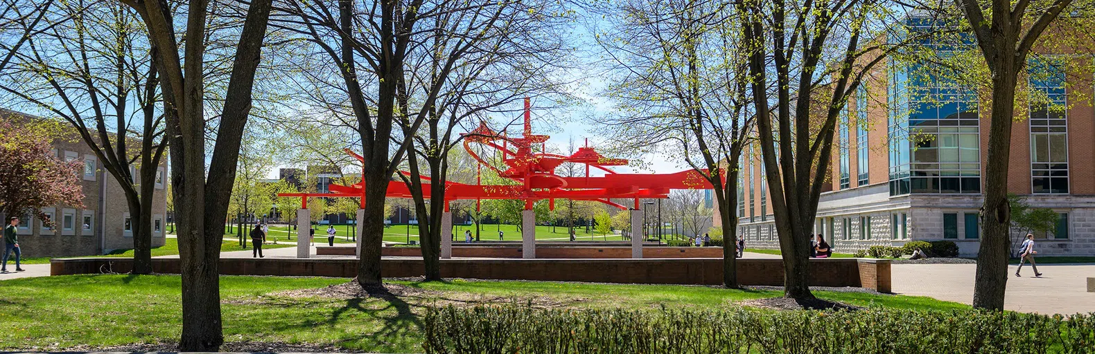 The image focuses on a sculpture on campus known as Turning Points, a large red sculpture in the center of campus. Students are walking around.