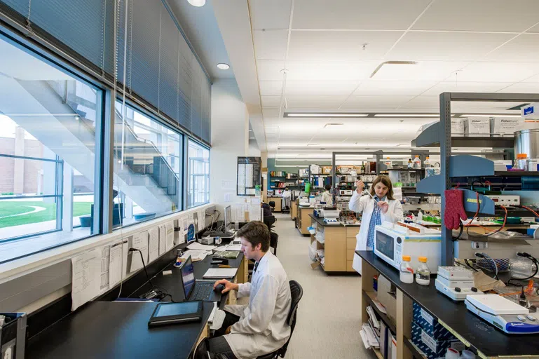 Students work in a science lab, one is on the computer and one is filling up a vial. 