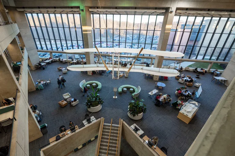 The image looks down on the library spaces where students are in groups and individually studying. A model of the Wright Brother's airplane hangs overhead.