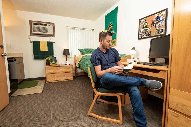 Student sitting at desk in single dorm room, working.