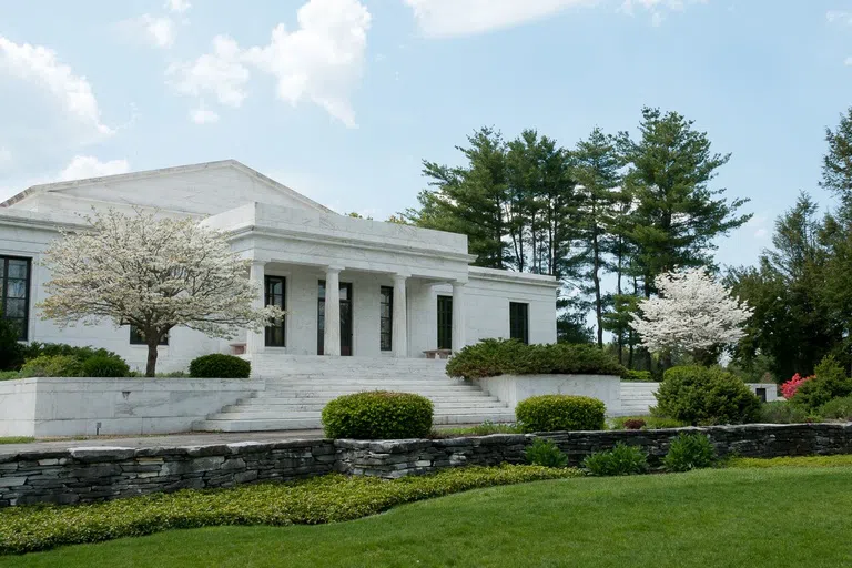 white museum building with columns, a grass lawn and trees