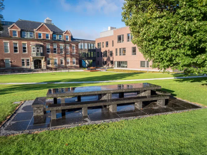 image of bench in front of corner of the science center where two buildings, one a red brick and another a more modern light wood building, meet.