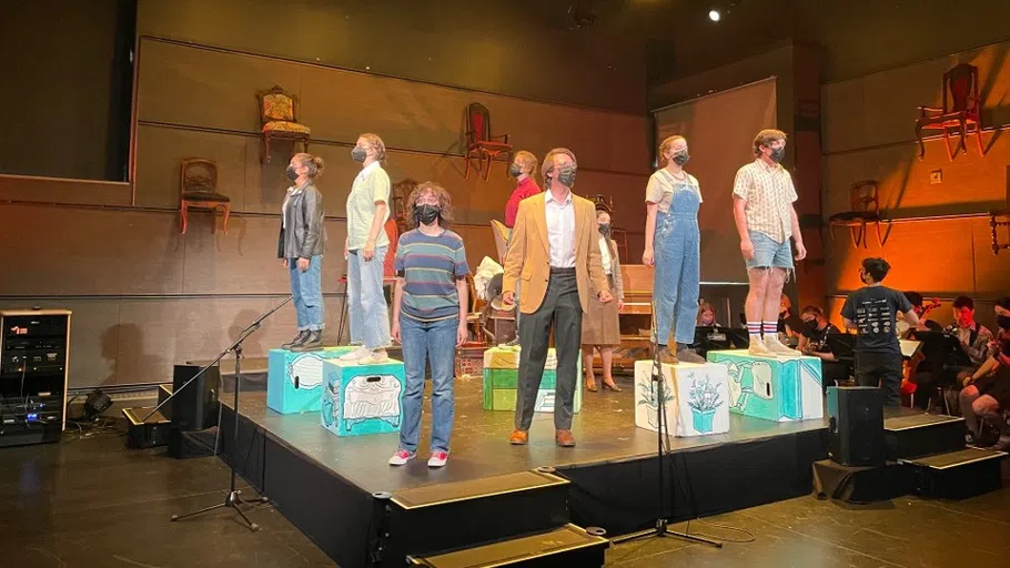 actors standing around a stage on boxes with chairs hanging from the back of the set