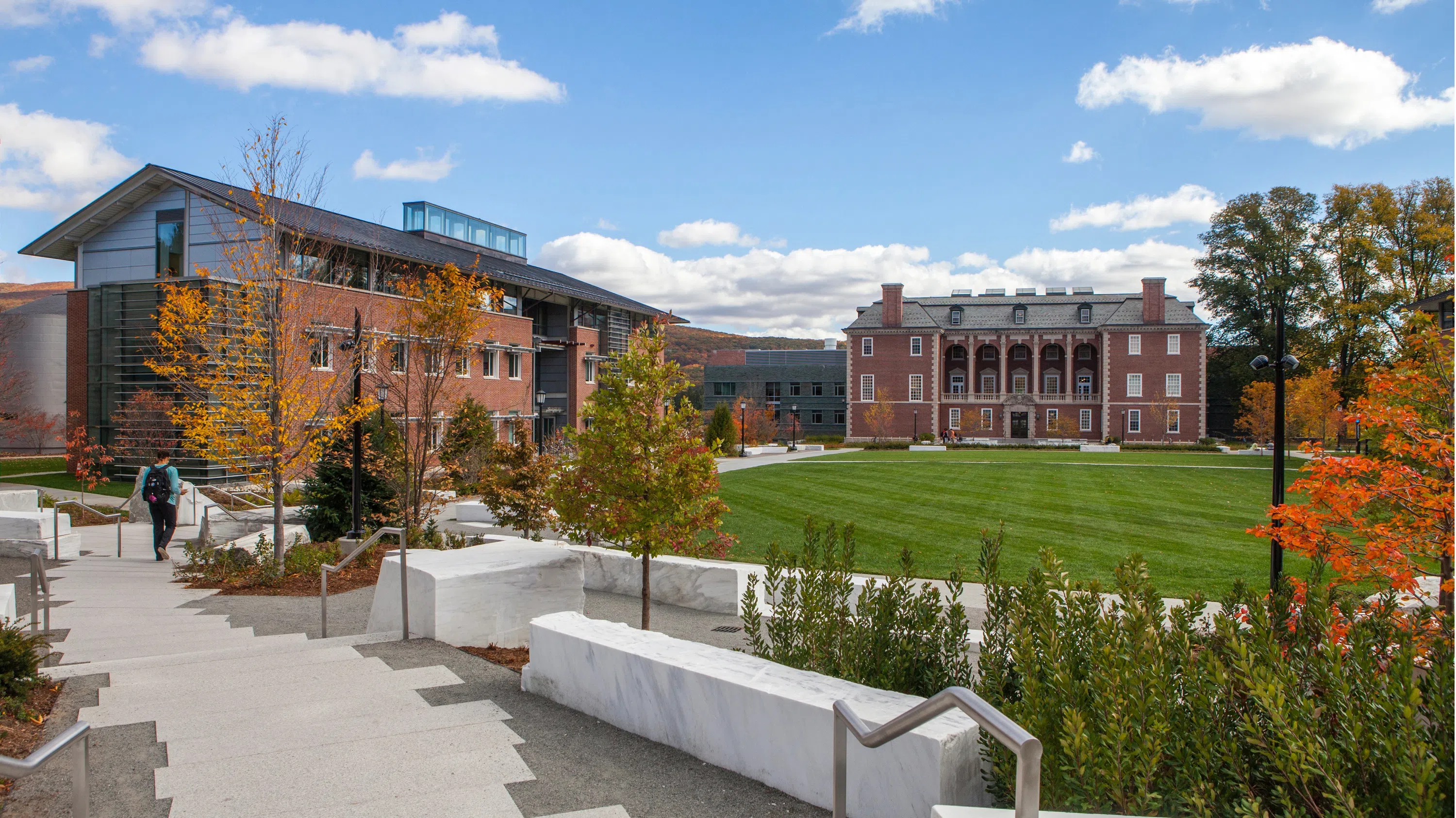 An image of Sawyer Quad, with marble benches in the foreground, a grassy quad area, Hollander Hall on the left, and Sawyer Library in the background.